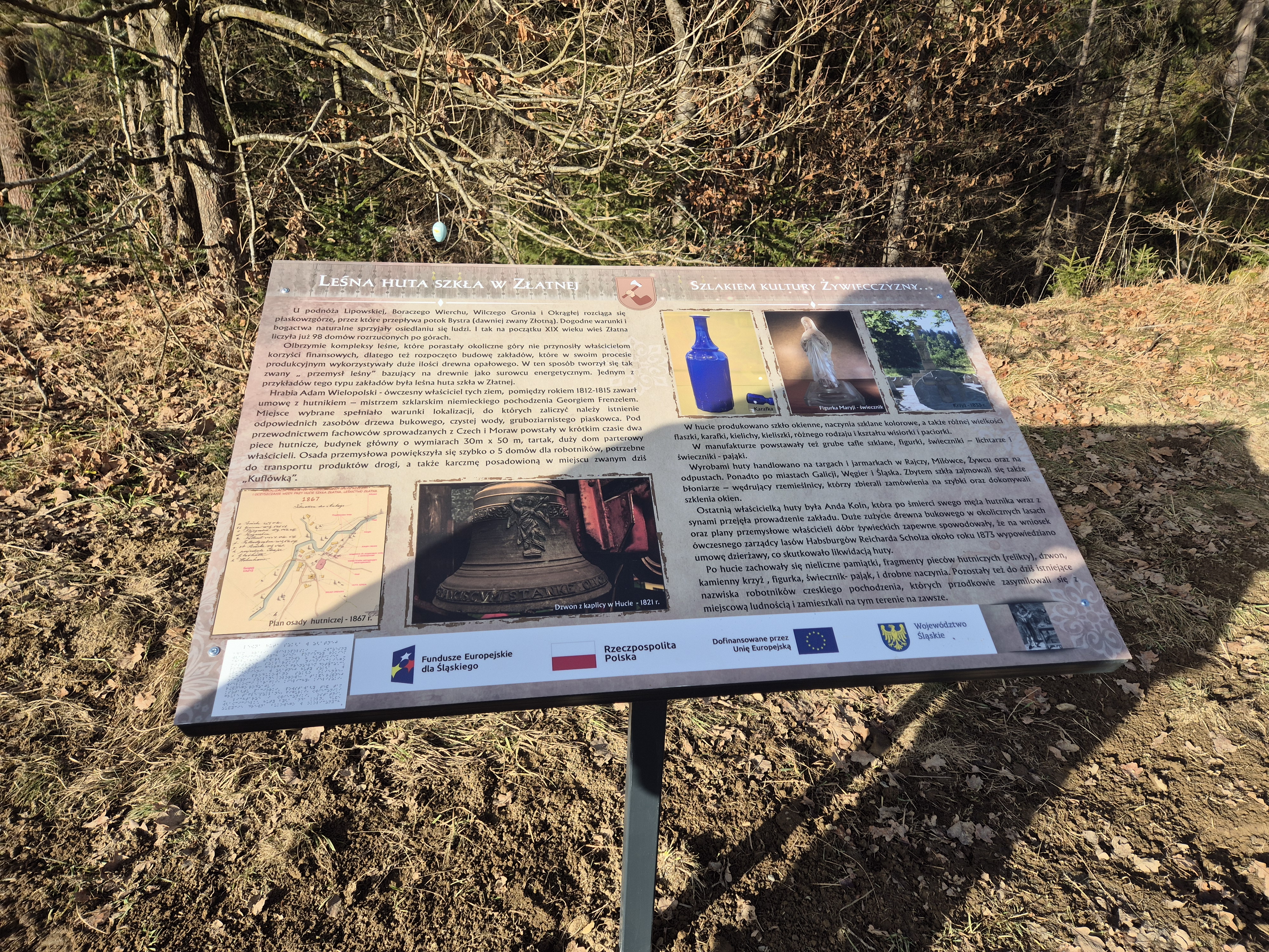 Fotografia przedstawia tablicę edukacyjną umieszczoną  na ścieżce historycznej prowadzącej do zabytkowej leśniczówki w Złatniej